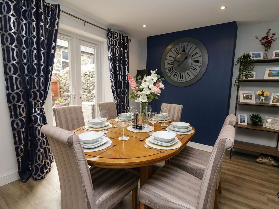 A dining room with a round table set and a clock on the wall at 6 Upperfield Street in Dolgellau