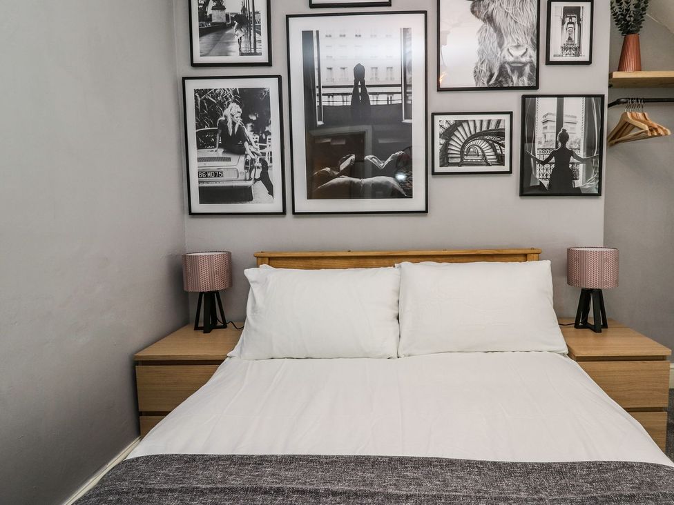 A bedroom with a bed, nightstand, lamp, and wall photo frames at 6 Upperfield Street in Dolgellau