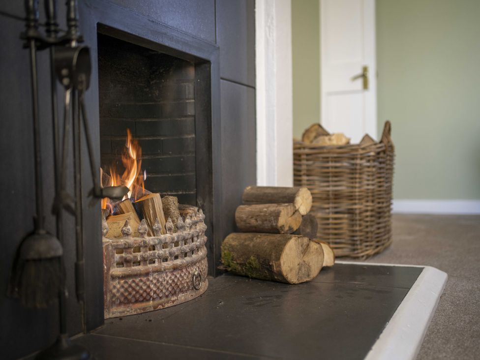 A fireplace with fire and logs at Clayhills Cottage in Blairgowrie