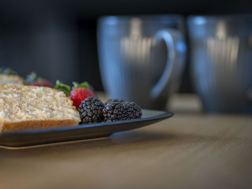 A plate with cake and berries with coffee cups in the background at Clayhills Cottage Blairgowrie