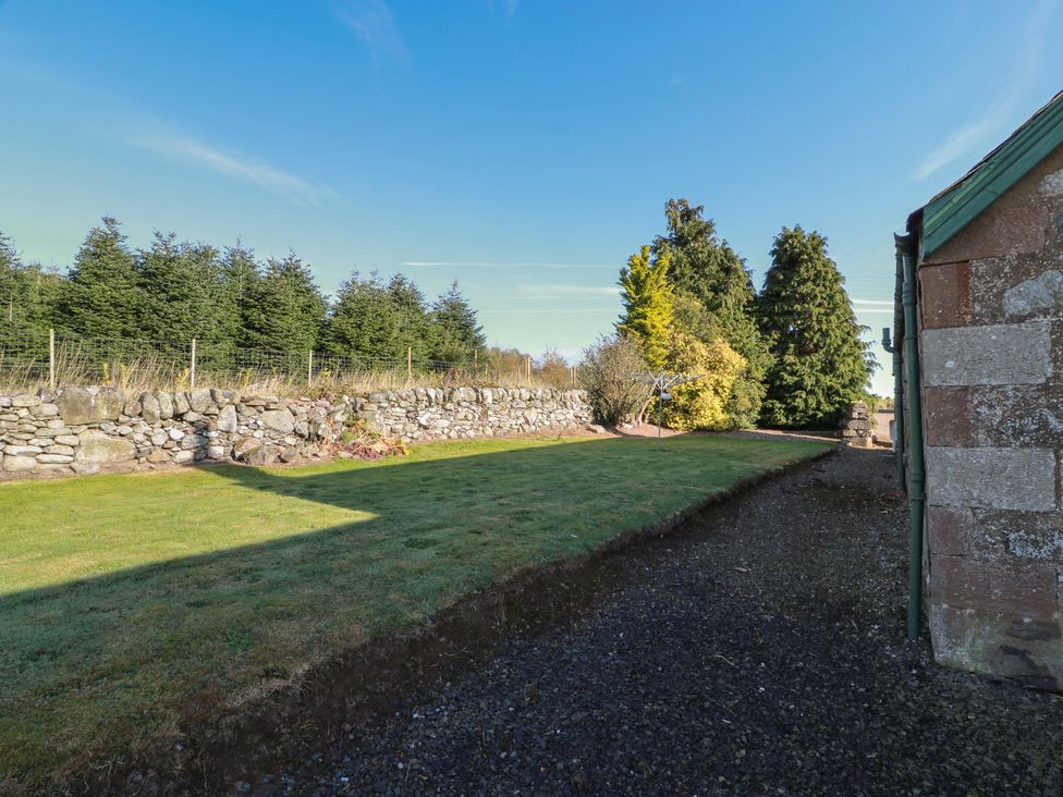 A garden with a stone wall and trees at The Bothy in Blairgowrie