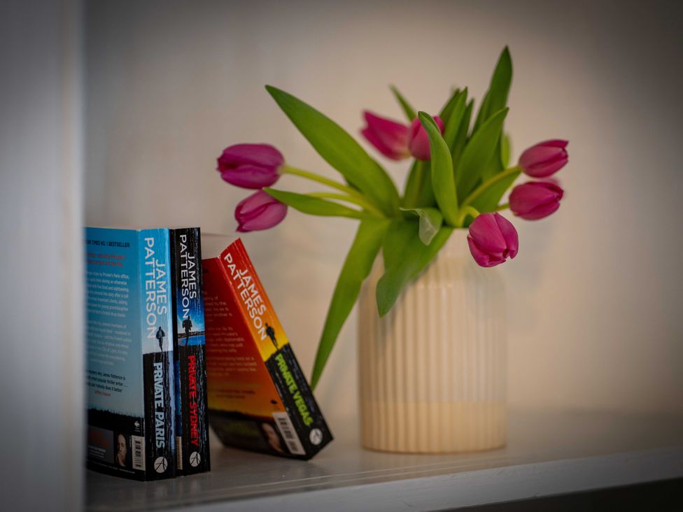 A vase with tulips beside books on a shelf at The Bothy in Blairgowrie