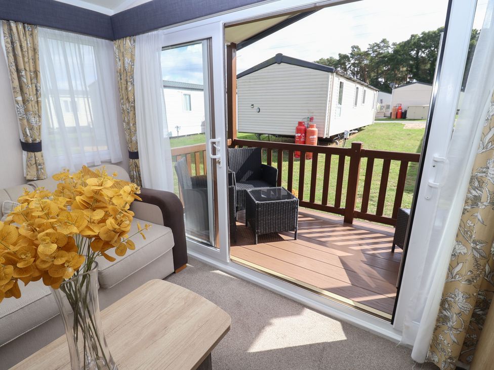 A living room with a view of a deck and flowers in a vase at Stag Lodge, Caravan 70 Great Yarmouth