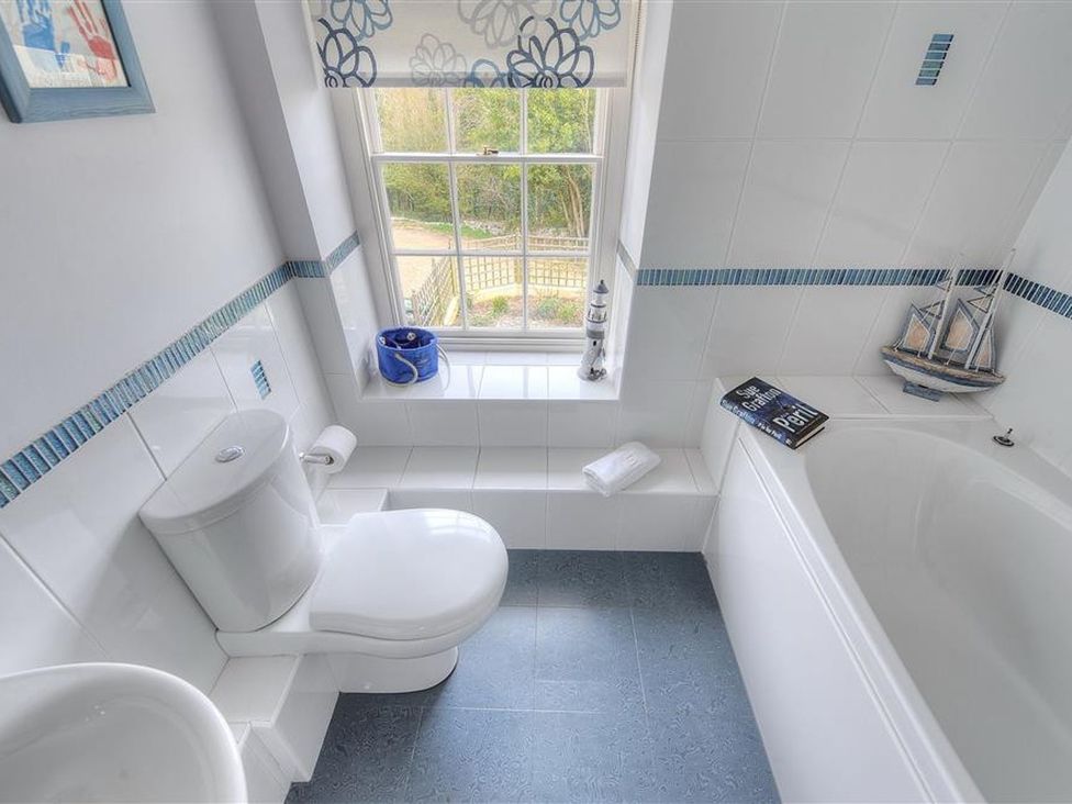 A bathroom with a toilet, bathtub, and a window at Half Moon Cottage in Lyme Regis