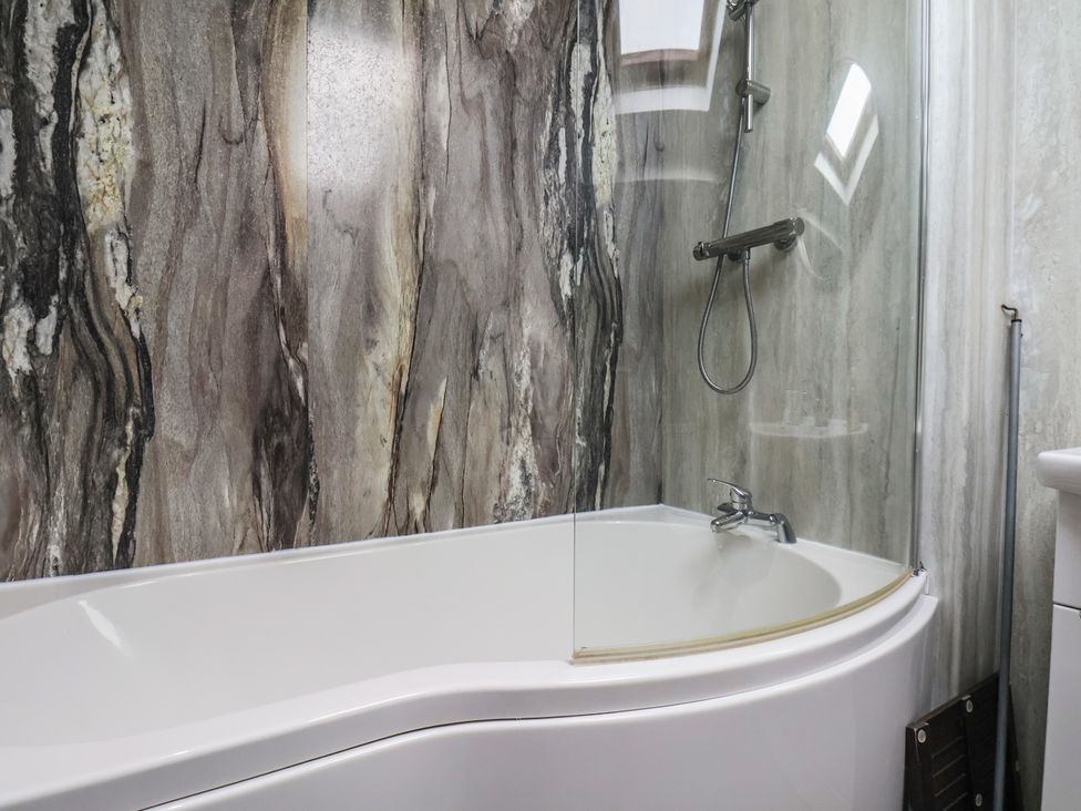 A bathtub with a shower and decorative wall at The Studio on the Crescent in Whitby