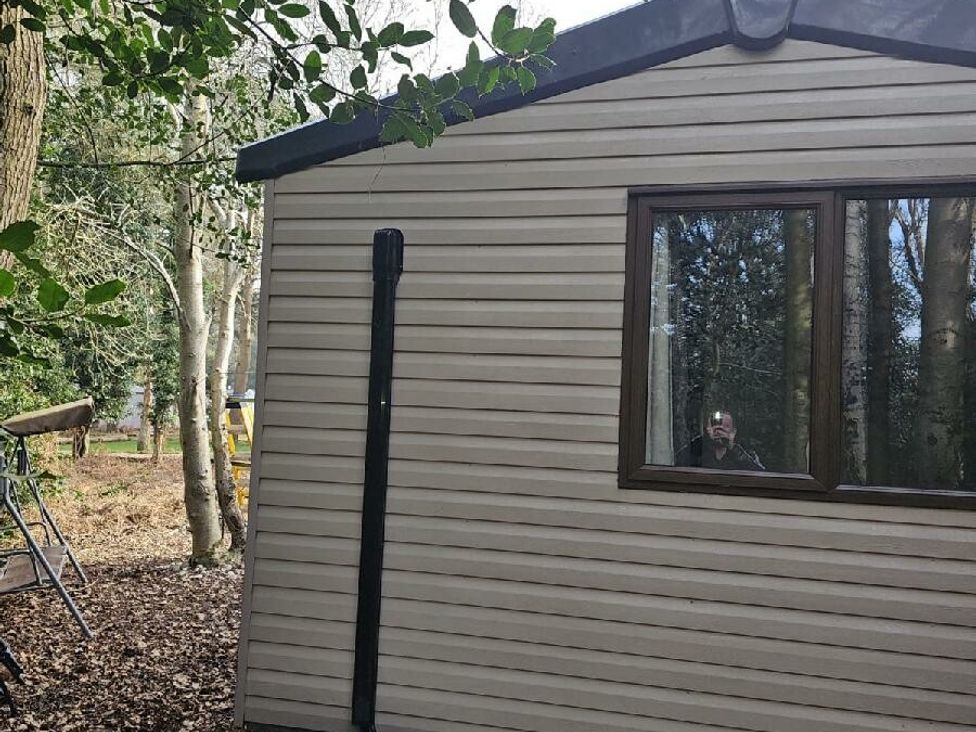 a cabin exterior with a window and trees surrounding it at Wild Duck Holiday Park - Holiday Accommodation 10389 Nr Great Yarmouth