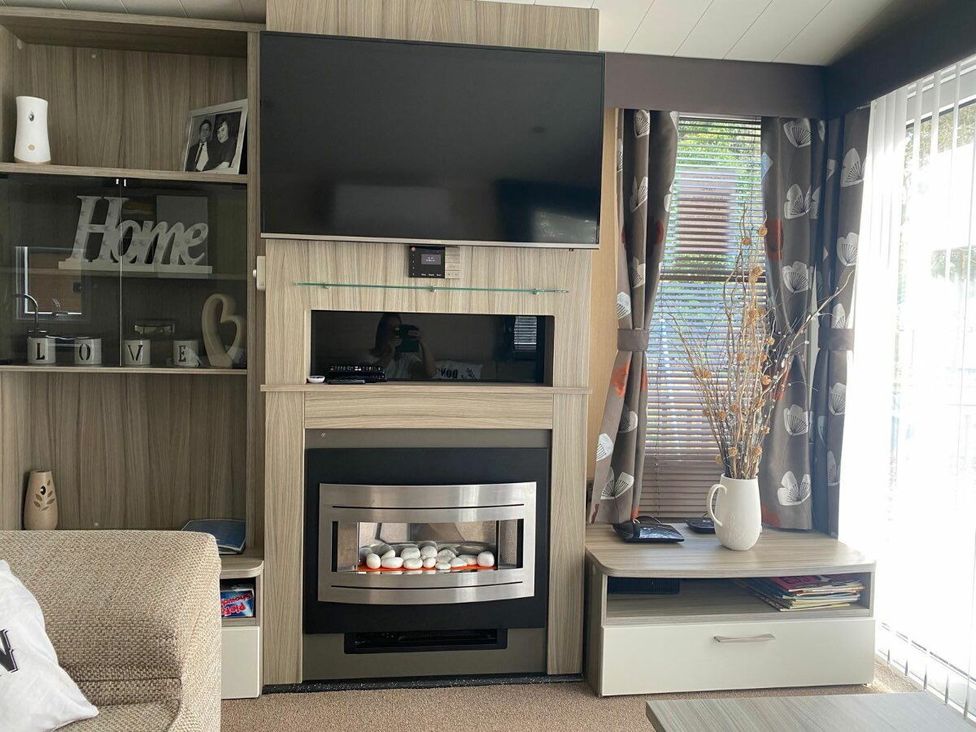 a living room with a television on a cabinet and a fireplace at Wild Duck Holiday Park - Holiday Accommodation 10389 Nr Great Yarmouth