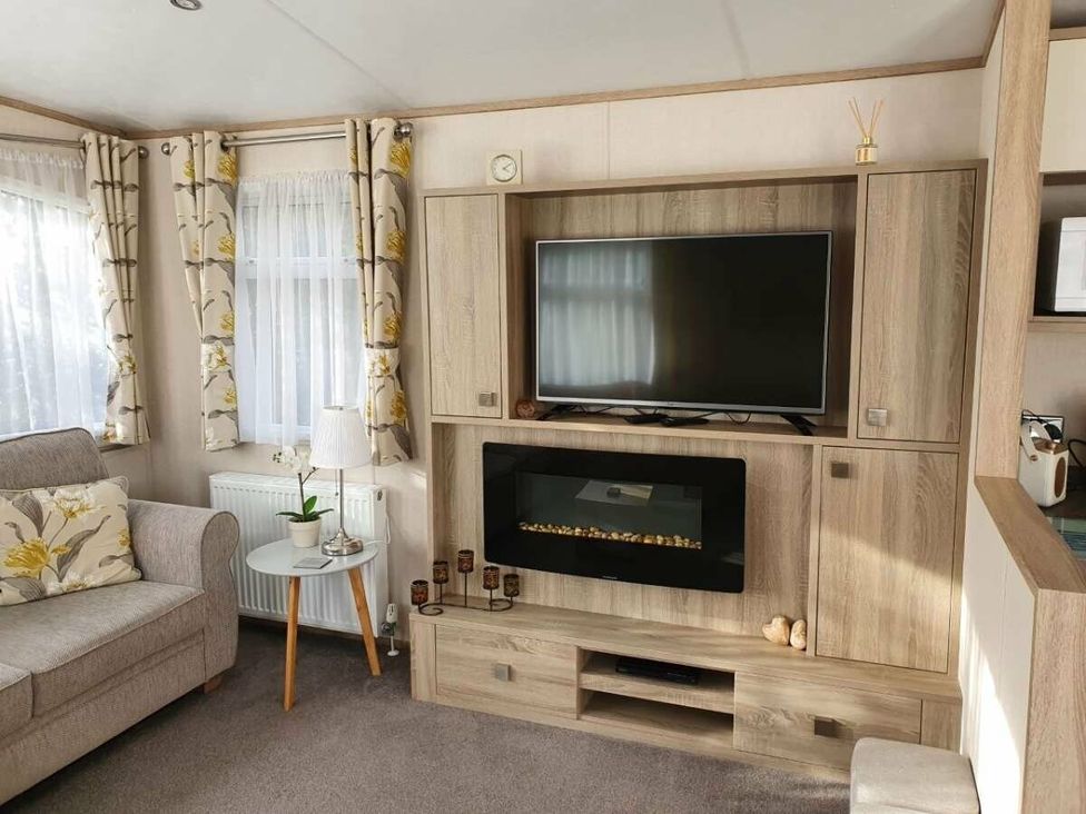a living room featuring a television mounted on a wooden cabinet with a fireplace at Shorefield Country Park - Holiday Accommodation 10821, Milford On Sea