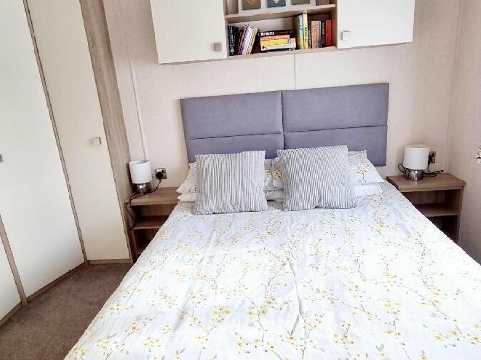 a bedroom with a bed, two bedside tables, and shelves at Shorefield Country Park - Holiday Accommodation 10821, Milford On Sea