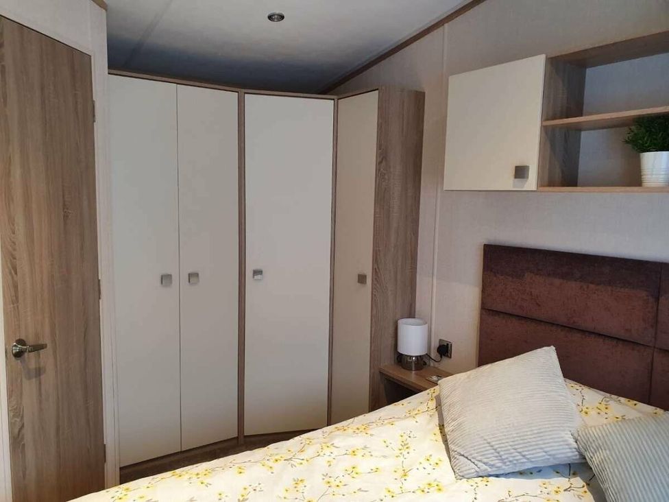 a bedroom with a bed covered in a floral blanket and built-in wardrobes at Shorefield Country Park - Holiday Accommodation 10821, Milford On Sea