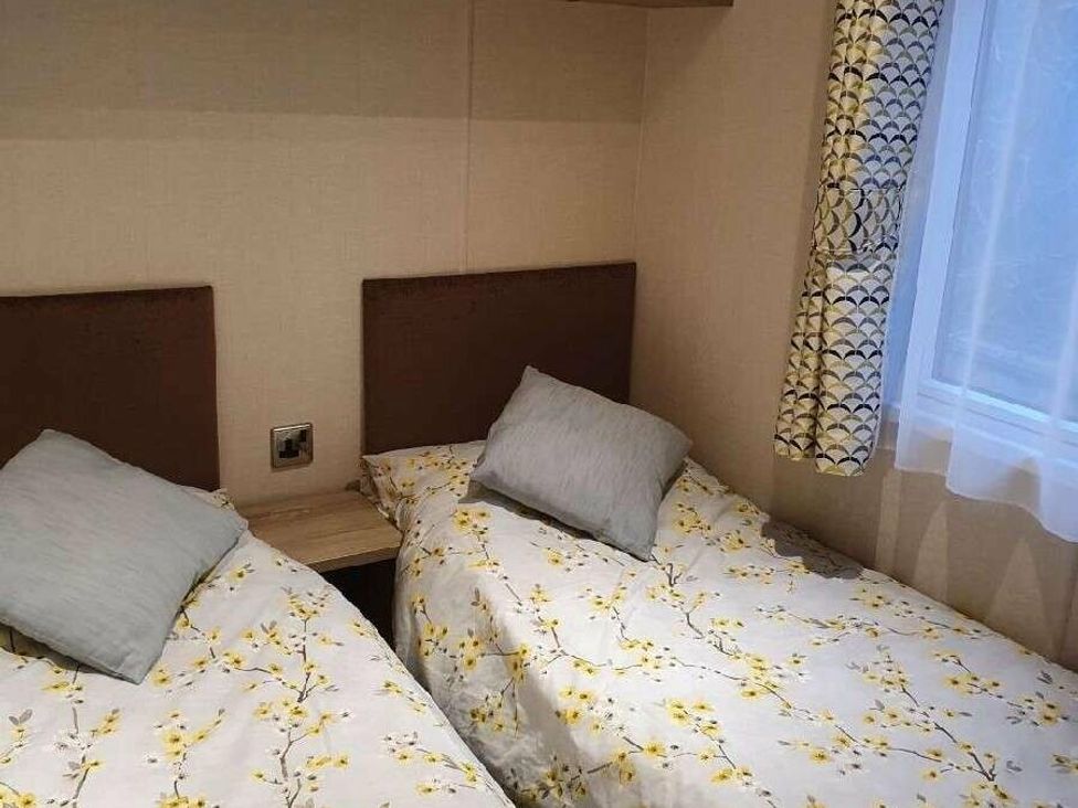 a bedroom with two single beds, light-colored bedding with floral patterns, and a window at Shorefield Country Park - Holiday Accommodation 10821, Milford On Sea