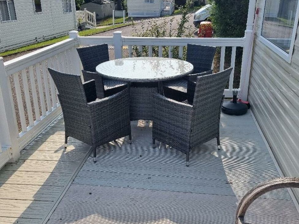 a deck with a round table surrounded by four wicker chairs at Shorefield Country Park - Holiday Accommodation 10821 in Milford On Sea