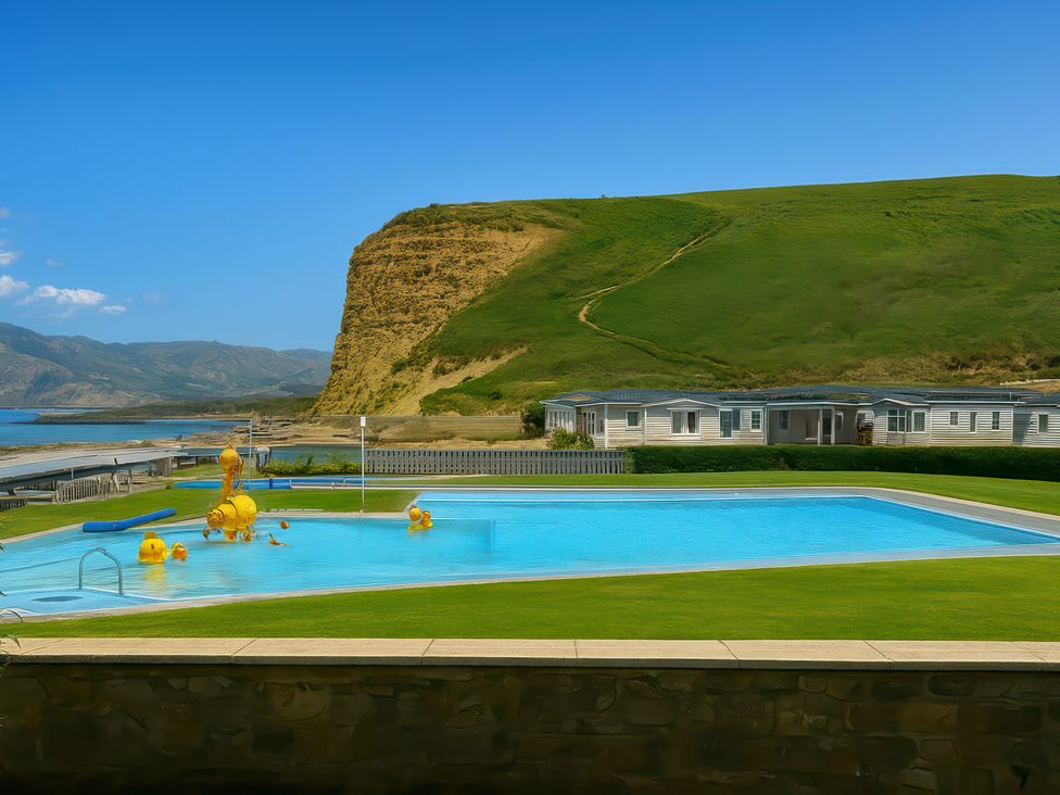a swimming pool with a grassy area and hillside in the background at Freshwater Beach Holiday Park - Holiday Accommodation 12281 in Burton Bradstock
