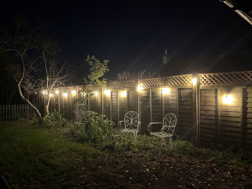 A garden with two chairs and lights on a fence at Maud Heath's Snug in Chippenham