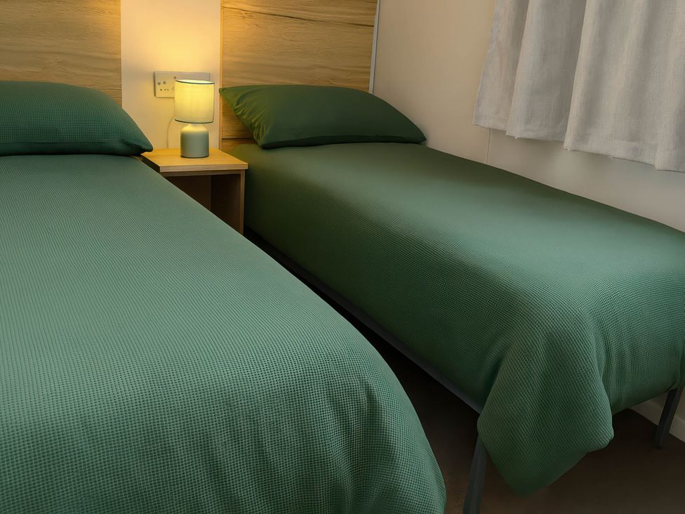 A bedroom with two single beds and a bedside lamp at Littlesea Holiday Park - Holiday Accommodation 13127 Weymouth