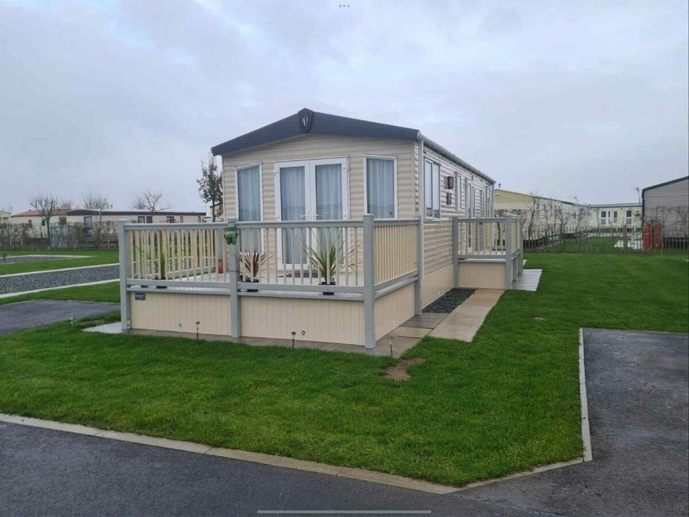 a mobile home with a deck surrounded by grass at Golden Palm Resort - Holiday Accommodation 13363, Skegness