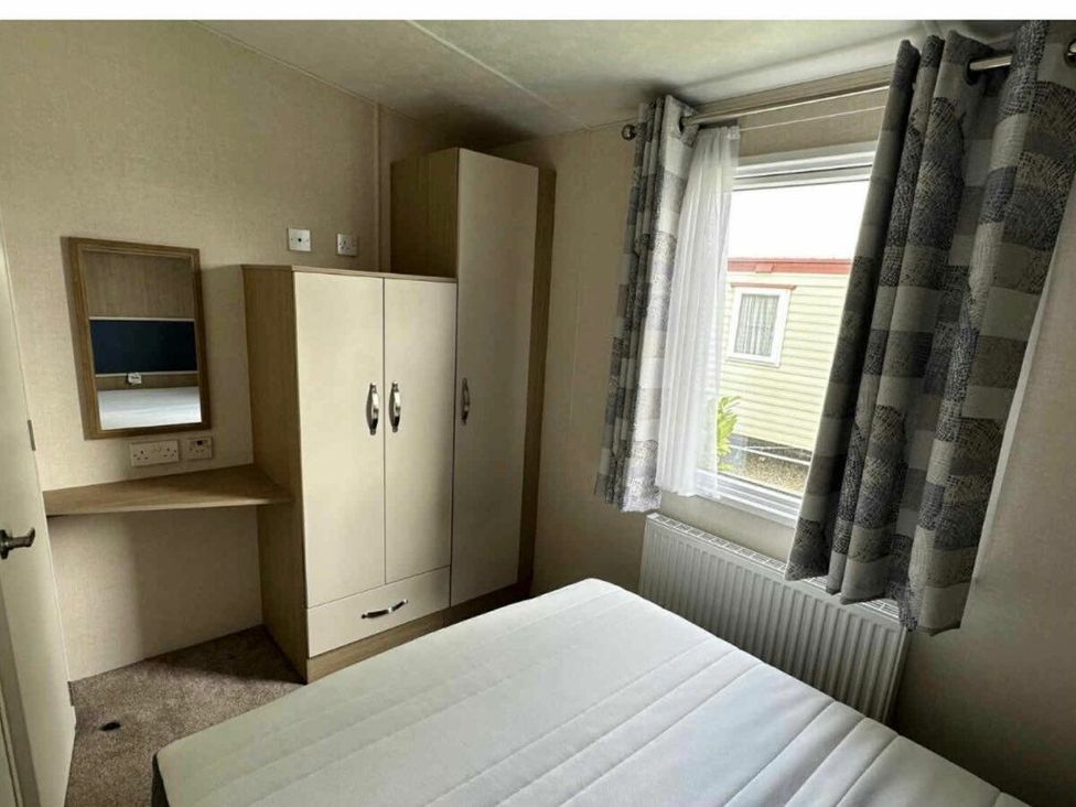 a bedroom with a bed, wardrobe, mirror, and window at Golden Palm Resort - Holiday Accommodation 13363, Skegness