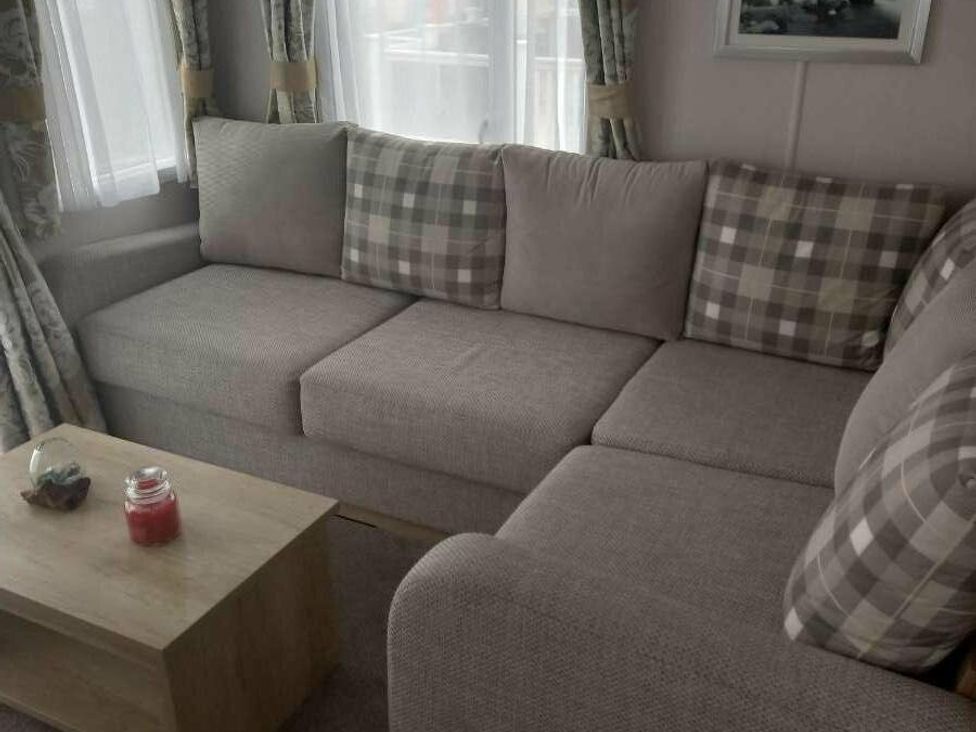 a sectional couch with checkered pillows and a wooden coffee table at Skegness Holiday Park - Holiday Accommodation 13968 in Skegness
