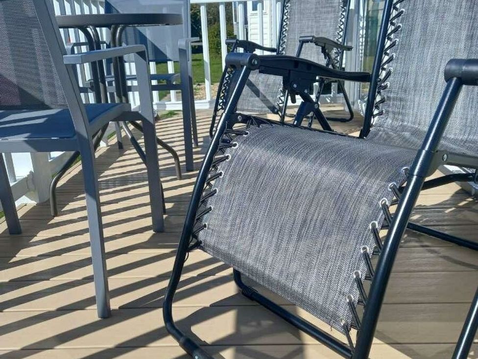 a gray reclining chair and dining set on a deck with sunlight casting shadows at Skegness Holiday Park - Holiday Accommodation 13968 in Skegness