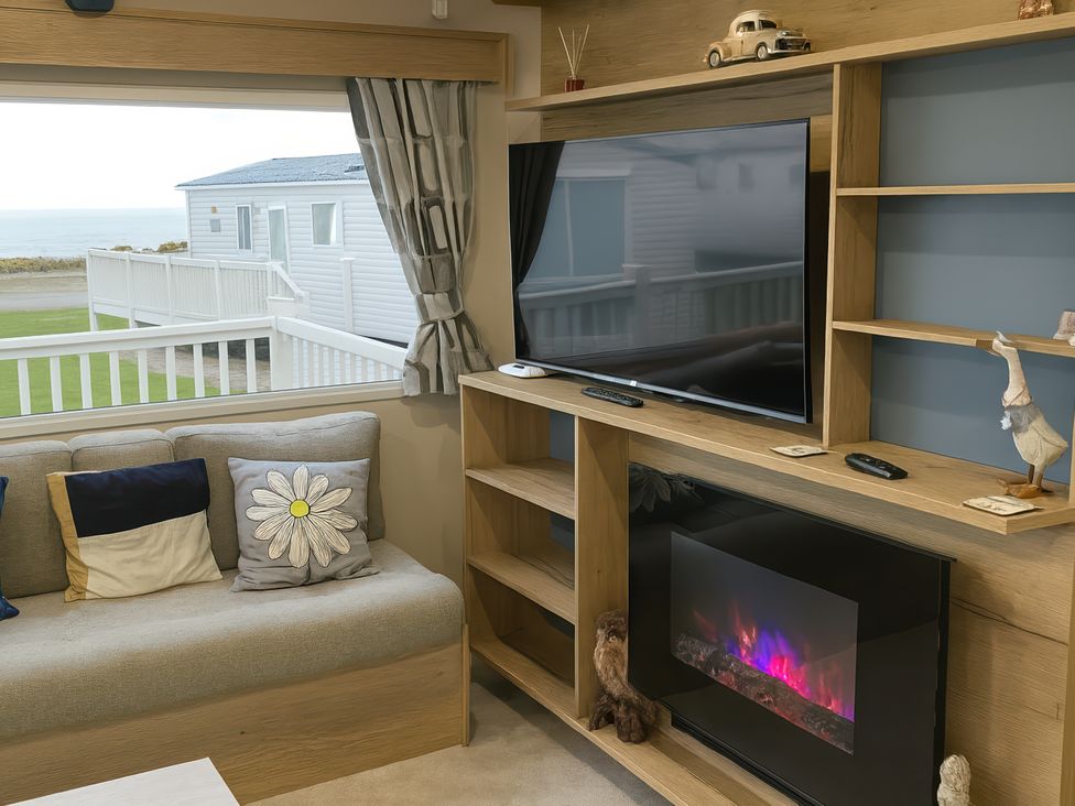 A living room with a television and electric fireplace at Reighton Sands Holiday Park - Holiday Accommodation 14875, Filey