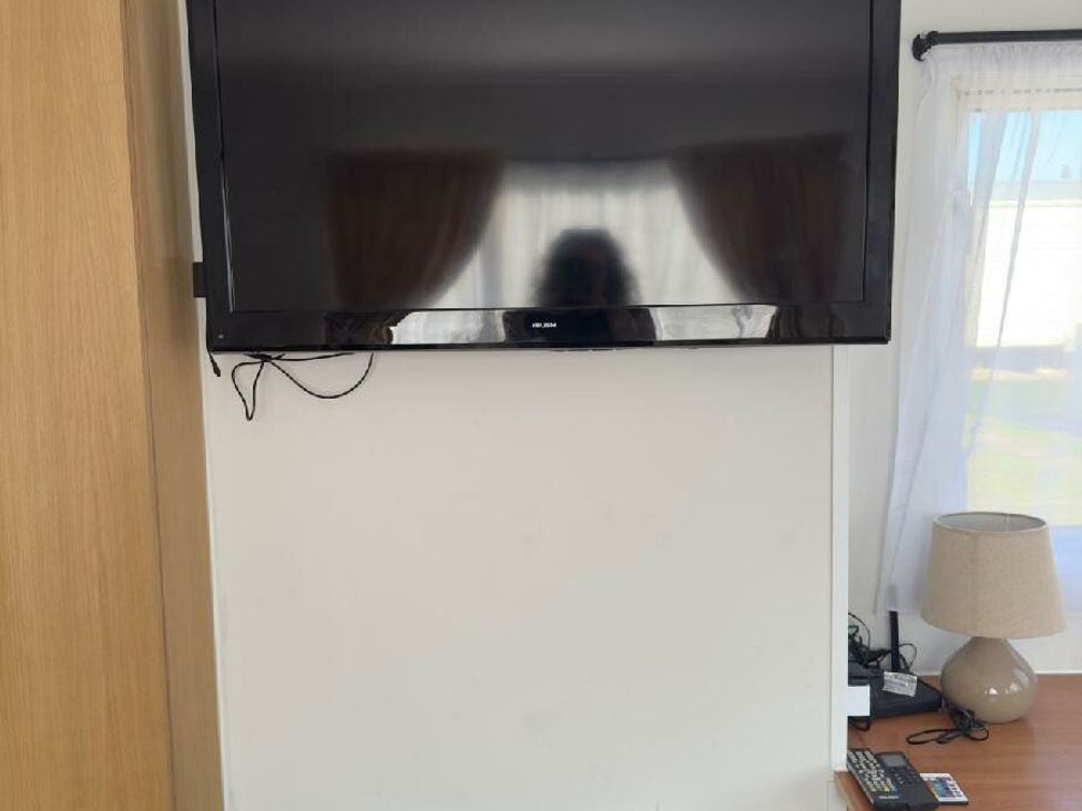 a wall-mounted television above a small table with a lamp at Sealands Caravan Park - Holiday Accommodation 15223 in Ingoldmells