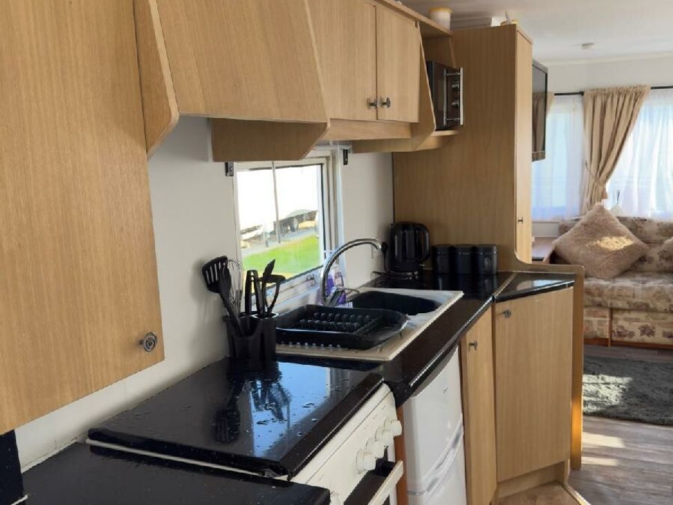 a kitchen with wooden cabinets and black countertops at Sealands Caravan Park - Holiday Accommodation 15223 in Ingoldmells