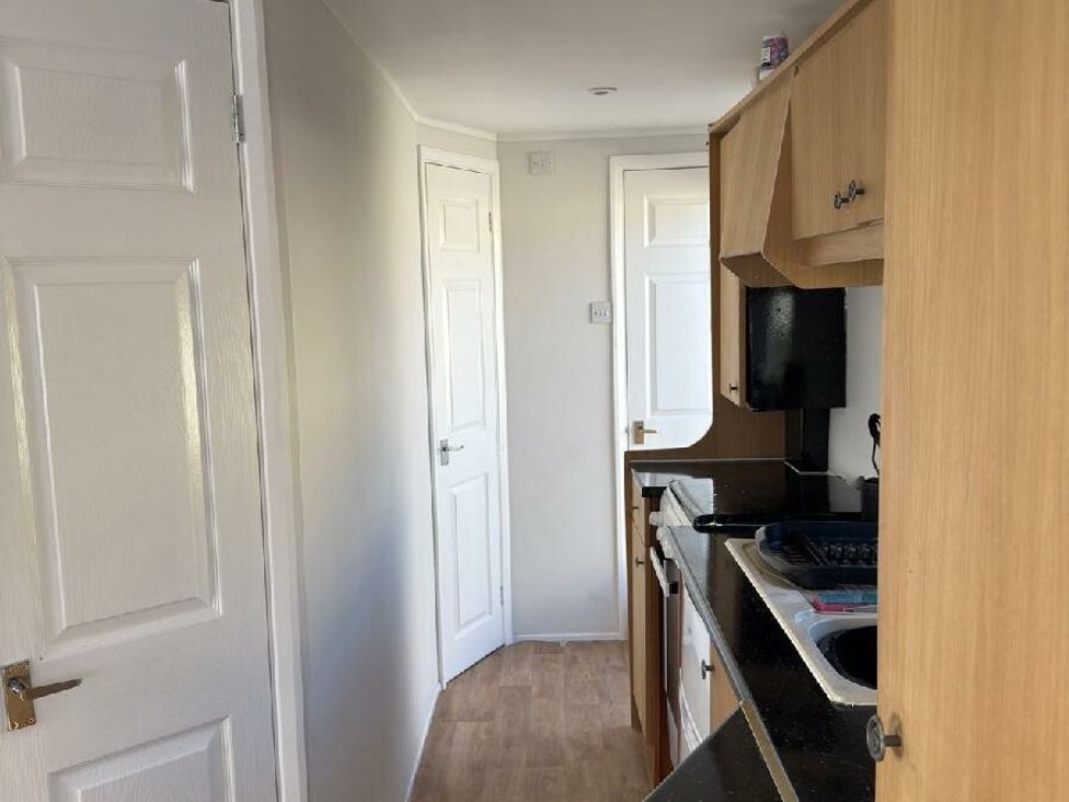 a kitchen area with wooden cabinets and a door at Sealands Caravan Park - Holiday Accommodation 15223 in Ingoldmells