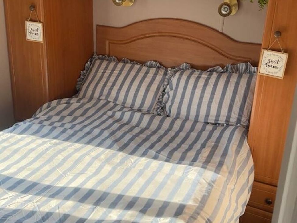 a bed with striped bedding and wooden headboard at Sealands Caravan Park - Holiday Accommodation 15223 in Ingoldmells
