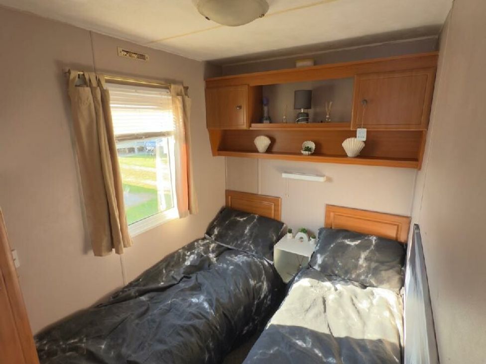 a bedroom with two single beds and a shelf above at Sealands Caravan Park - Holiday Accommodation 15223 in Ingoldmells