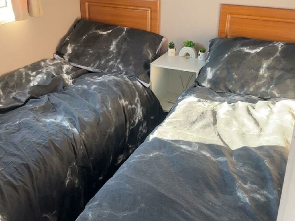 two beds with dark patterned bed linens and a bedside table at Sealands Caravan Park - Holiday Accommodation 15223 in Ingoldmells