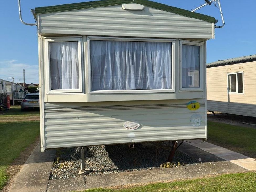 a static caravan with white curtains situated on a grassy area at Sealands Caravan Park - Holiday Accommodation 15223 in Ingoldmells