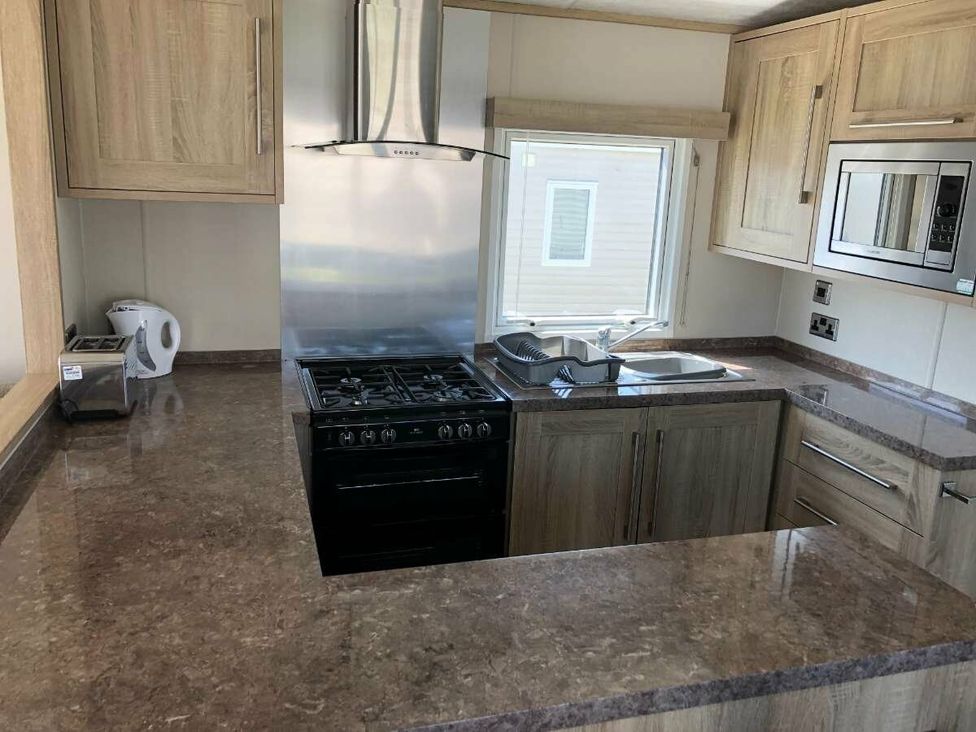 a kitchen with wooden cabinets and appliances at Hopton Holiday Village - Holiday Accommodation 15473, Great Yarmouth