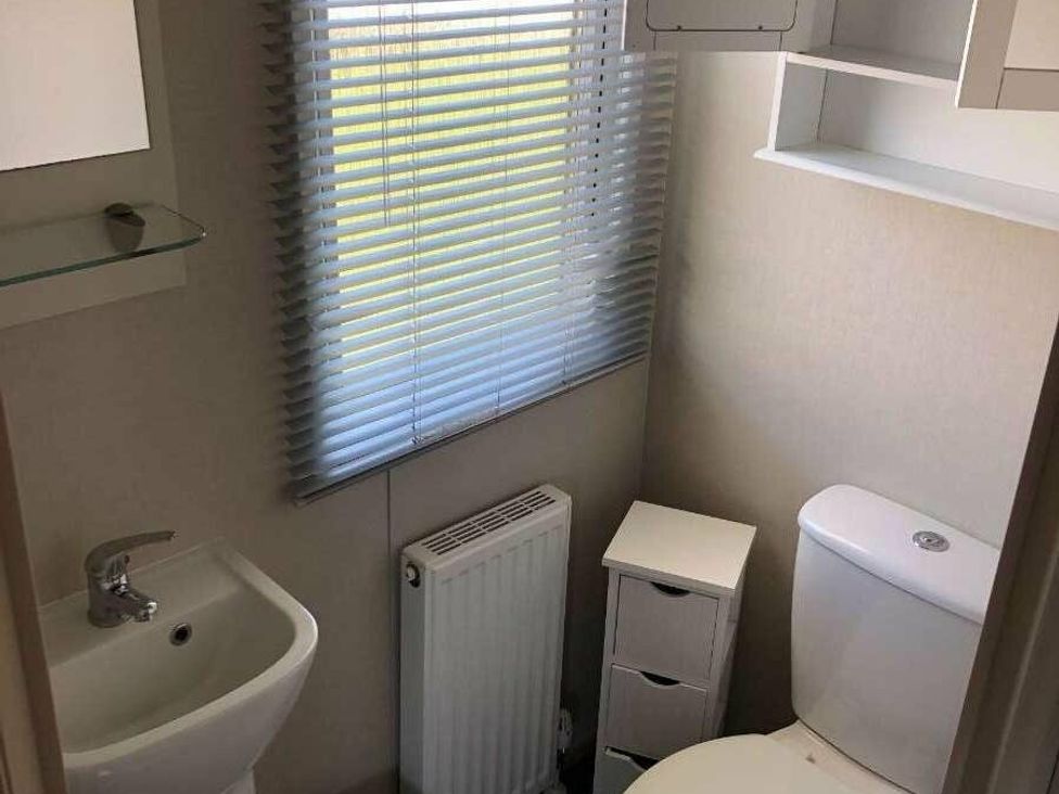 a bathroom with a sink, toilet, radiator, and window with blinds at Hopton Holiday Village - Holiday Accommodation 15473, Great Yarmouth