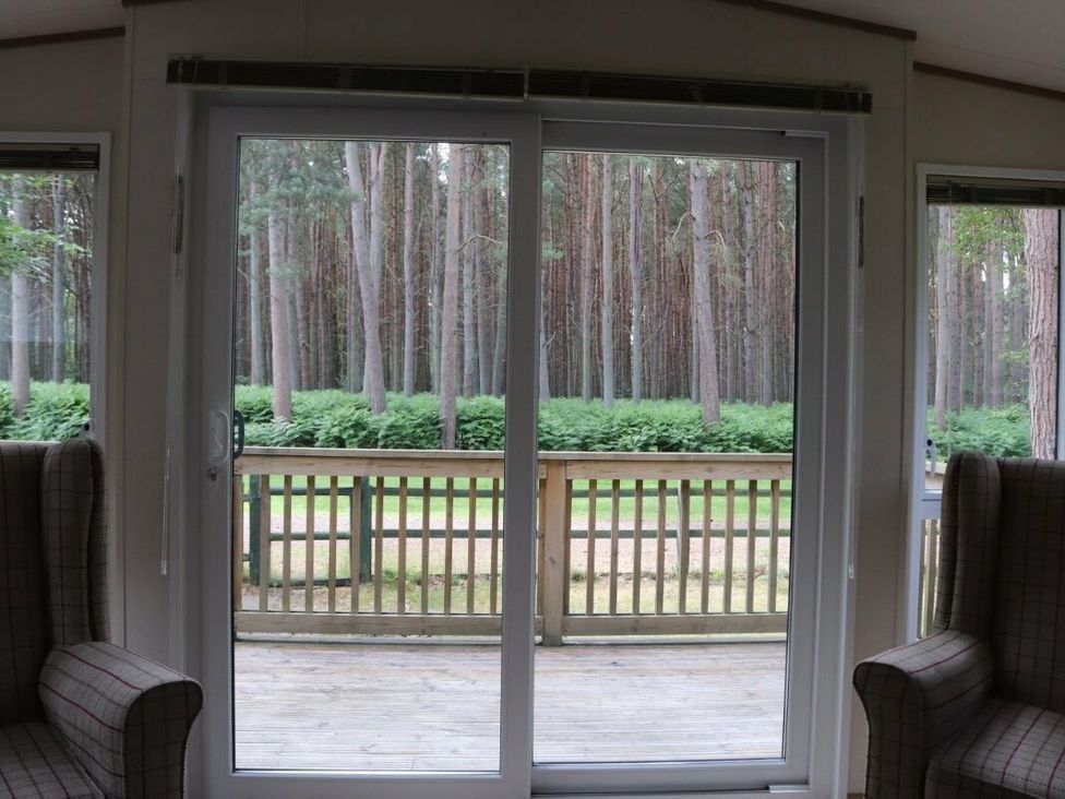 a view through glass doors showing trees and a deck area at Kelling Heath Holiday Park - Holiday Accommodation 15488 in Weybourne