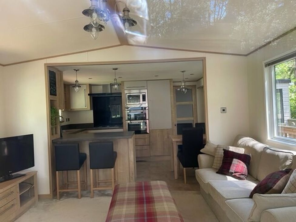 a living room with a sofa and television, open to a kitchen area at Kelling Heath Holiday Park - Holiday Accommodation 15488, Weybourne