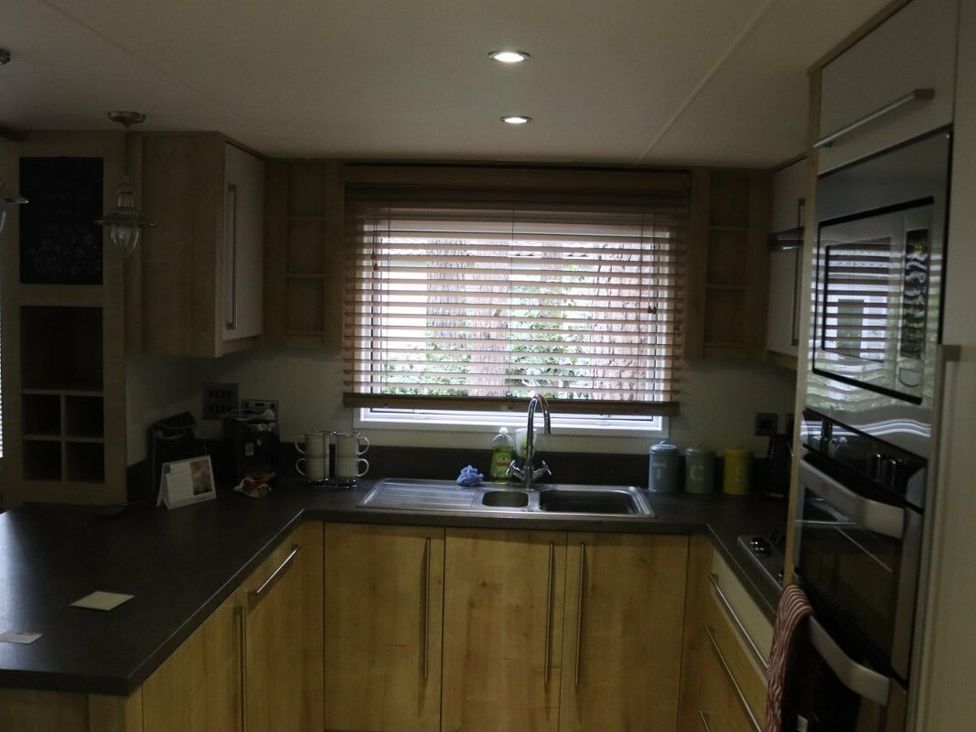 a kitchen with wooden cabinets and a sink near a window at Kelling Heath Holiday Park - Holiday Accommodation 15488 Weybourne