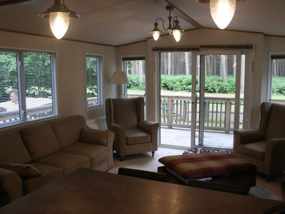 a living room with two armchairs, a sofa, and windows overlooking a deck at Kelling Heath Holiday Park - Holiday Accommodation 15488, Weybourne