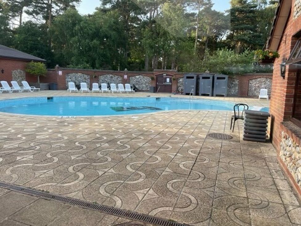 a swimming pool surrounded by tiled flooring and lounge chairs at Kelling Heath Holiday Park - Holiday Accommodation 15488 Weybourne