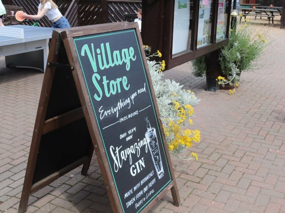 an A-frame sign displaying information about a village store and gin at Kelling Heath Holiday Park - Holiday Accommodation 15488 Weybourne