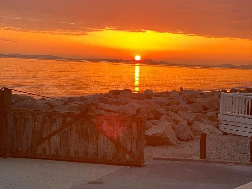 a sunset over the ocean with rocks in the foreground at Lyons Sunnysands Holiday Park - Holiday Accommodation 15526 Barmouth