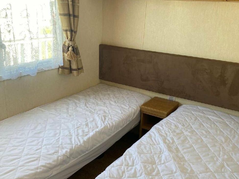 a bedroom with two single beds and a small bedside table at Lyons Sunnysands Holiday Park - Holiday Accommodation 15526 Barmouth