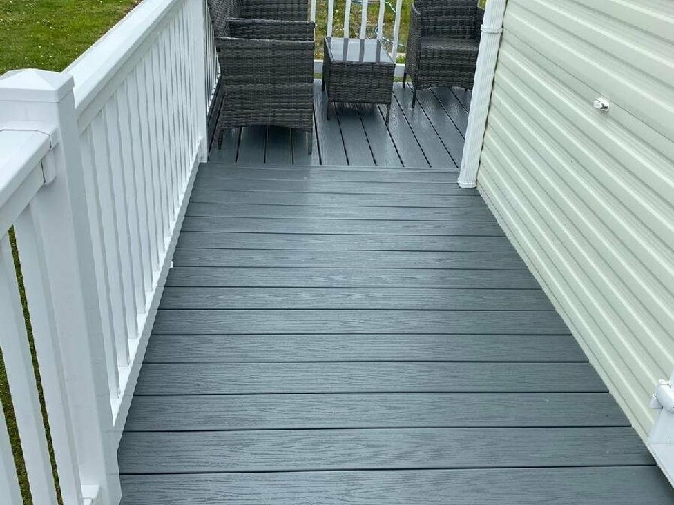 a gray deck with two wicker chairs and a small table at Lyons Sunnysands Holiday Park - Holiday Accommodation 15526 in Barmouth