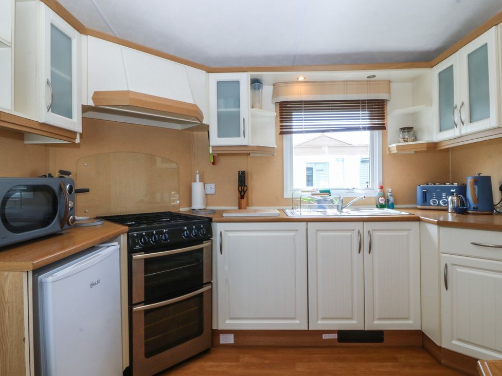 A kitchen with a microwave, oven, and sink at Sunnysands in Talybont near Barmouth