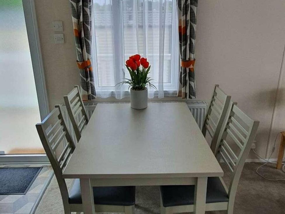 a dining table with chairs and a bouquet of flowers at Shorefield Country Park - Holiday Accommodation 15558 in Milford On Sea