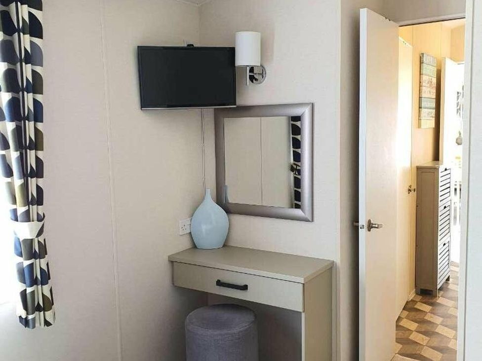a room with a wall-mounted TV, a mirror above a table, and a door at Shorefield Country Park - Holiday Accommodation 15558, Milford On Sea