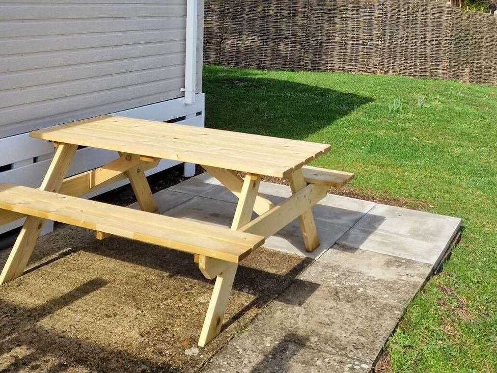 a picnic table on a patio with grass and a woven fence at Shorefield Country Park - Holiday Accommodation 15558 Milford On Sea