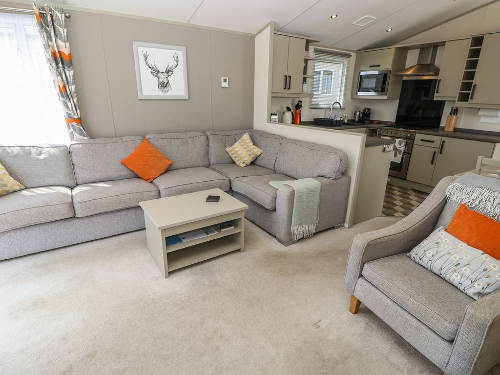A living room with a sofa and kitchenette at Pine Tree Lodge - Shorefield Country Park in Milford On Sea