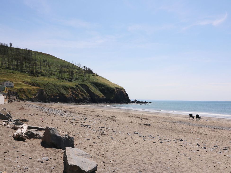 A beach with sand, rocks, and chairs at Captain's Cabin in Clarach Bay near Aberystwyth