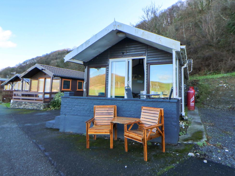 An outdoor area with a cabin, wooden chairs, and a table at Captain's Cabin in Clarach Bay near Aberystwyth