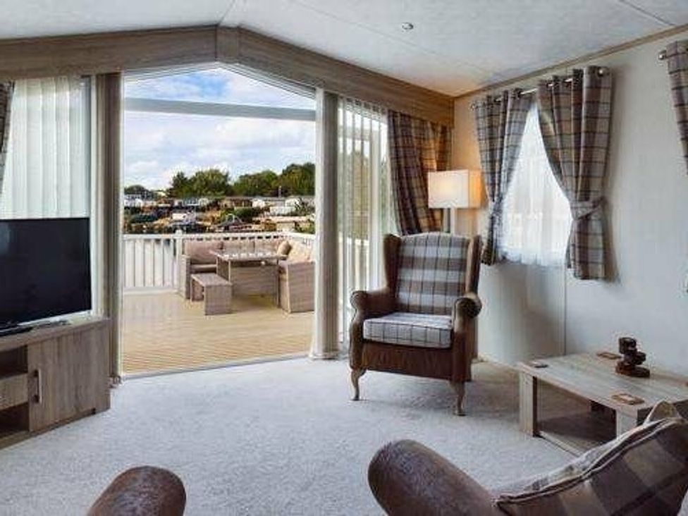 a living room with a TV and a chair leading to a deck at Tattershall Lakes Country Park - Holiday Accommodation 16408, Tattershall